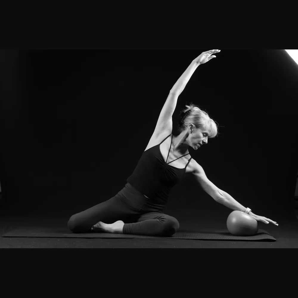 Florence in a seated side stretch with a Pilates ball