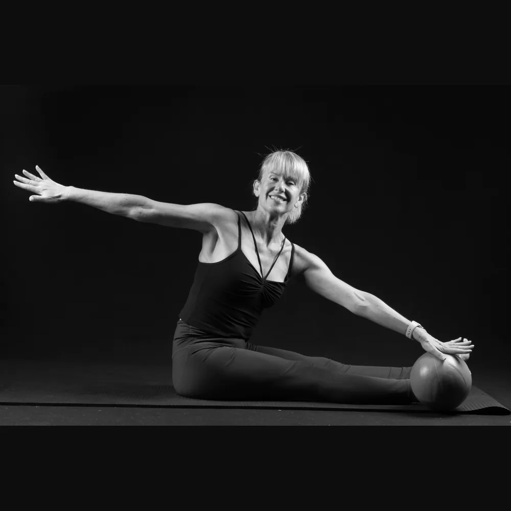 Florence smiling in a seated mermaid stretch with a Pilates ball